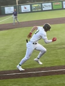 Baseball player in white uniform with green trim running on a baseball field.