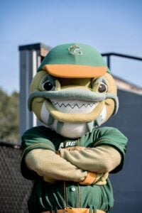 Mascot in a green baseball uniform with orange trim, wearing a green baseball cap with a fish logo.