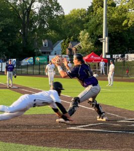 Baseball player slides into home plate as catcher prepares to tag him out.