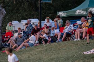 People watch an outdoor event from lawn chairs, some wearing "Cape Catfish" gear.