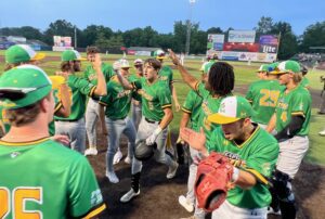 Baseball team celebrates victory on the field, wearing green and yellow uniforms.
