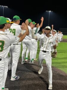 Baseball team in white uniforms and green hats celebrates with high fives on a field at night.