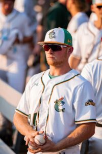 Baseball player in uniform and sunglasses holding two baseballs, looking away.