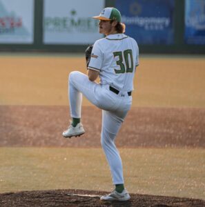 Baseball pitcher in white uniform with green accents and number 30 on back, mid-throw on mound.