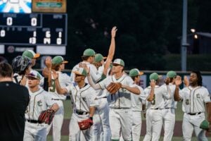 Baseball players in green and white uniforms celebrate on the field with hands raised.