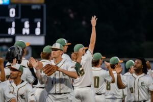 Baseball players in uniform celebrate after a game, with scoreboard in background.