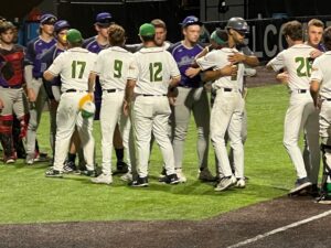 Baseball players in white and green uniforms hug on a field, celebrating a win.