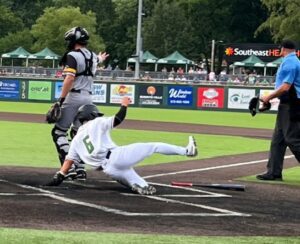 Baseball player slides into home plate as catcher looks on; umpire stands nearby.