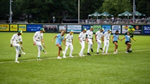 Baseball players and dancers perform a routine on a green field with advertisements in the background.