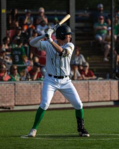 Baseball batter in white uniform and green socks ready to hit in a stadium.