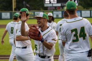 Baseball players in white and green uniforms celebrate on a field, one with a red glove giving a high-five.