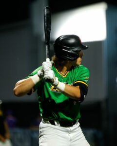 Baseball player in green uniform and black helmet at bat, holding a black bat.