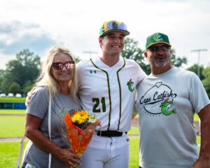Baseball player with parents on field, holding flowers.