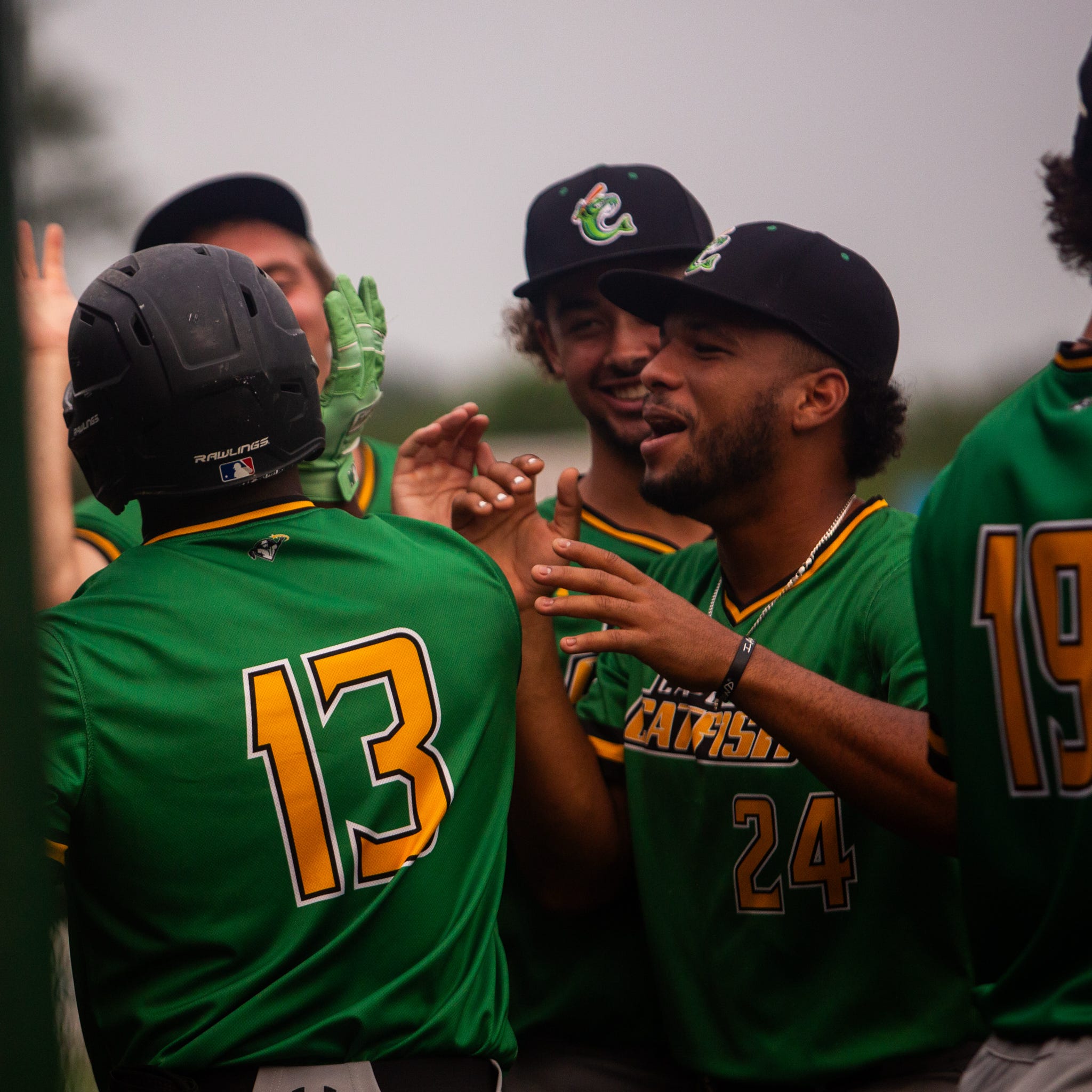 Baseball players in green jerseys celebrate with high-fives after a game.